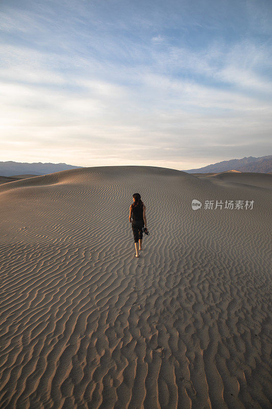 美丽的年轻女子走向纹理沙丘看太阳与蓝天在死亡谷