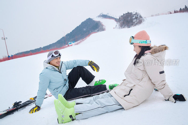 快乐的青年伴侣坐在雪地上闲聊