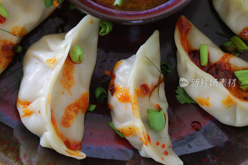 这是蒸饺(南亚饺子)的特写图片，白面粉和水面团里裹着鸡肉和什锦蔬菜，淋上辣椒油，放在盘子里，周围是用橙子辣酱做的小模子