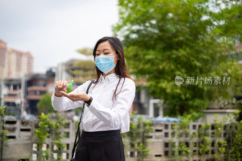 年轻的亚洲妇女戴医用口罩，在工作前用酒精洗手液洗手