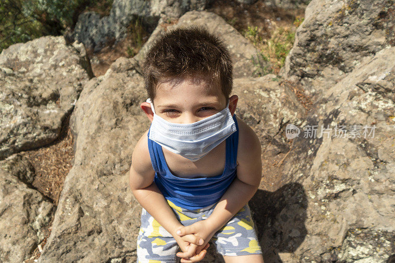 为了避免冠状病毒Covid-19，男孩试图戴着外科口罩晒太阳并微笑着对着镜头