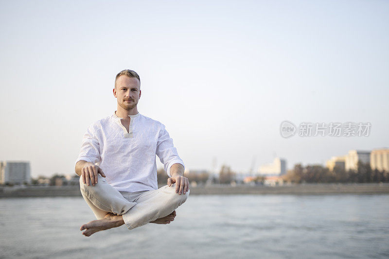 年轻美丽的男子在半空中沉思的肖像，漂浮在户外地面上，坐在莲花姿势，莲花身