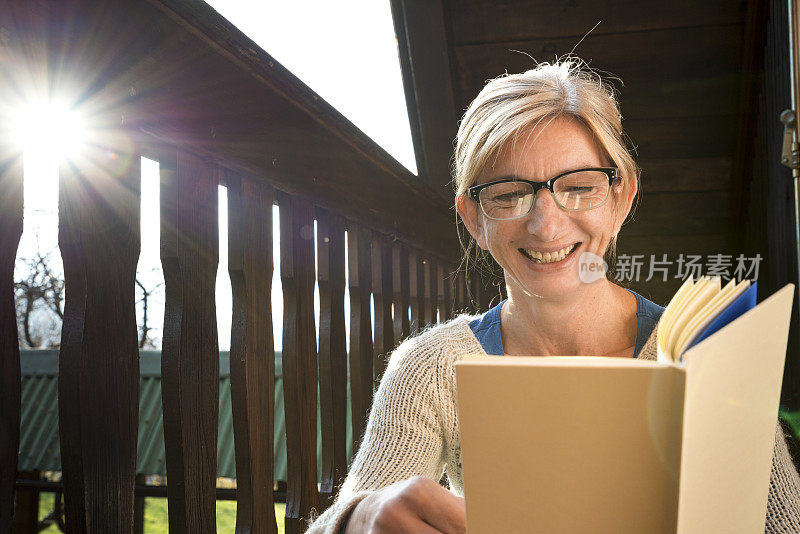 一个女人在阳台上放松，看书，享受秋高气爽的周日下午