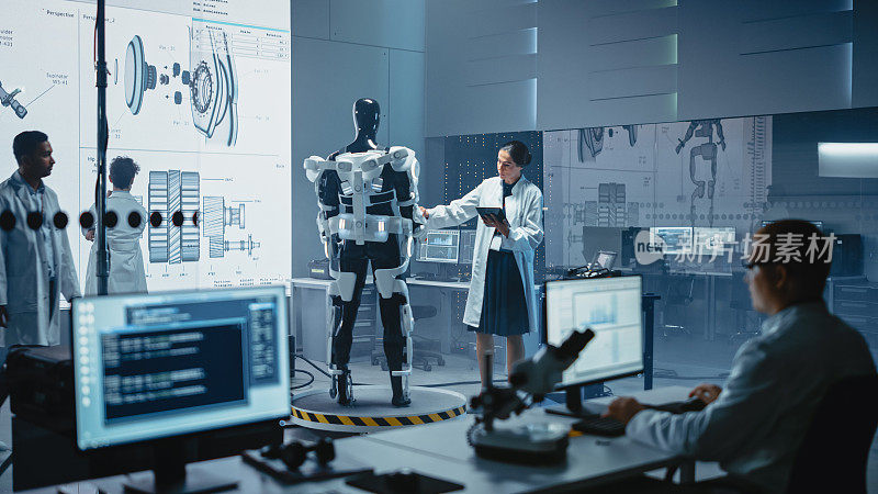 机器人开发实验室:女科学家使用数字平板电脑，研究机器人外骨骼原型。工程师设计Exosuit来帮助残疾人，工人举起货物