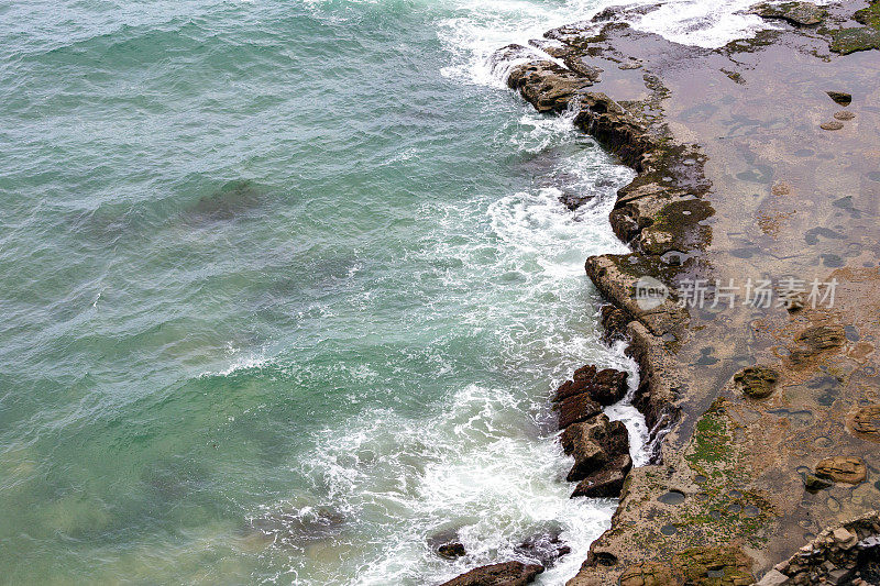 Arial视图的波浪打破到一个岩石的海岸线，背景与复制空间