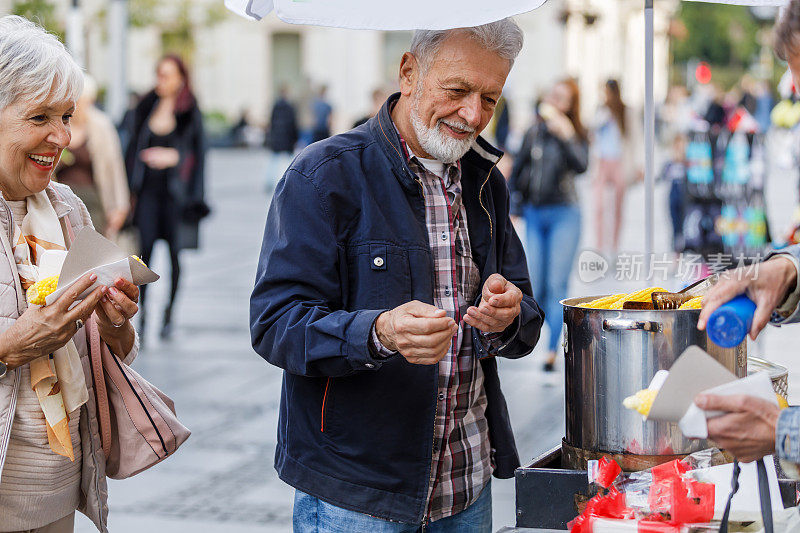 一对老年夫妇在城市街道上吃玉米的肖像。