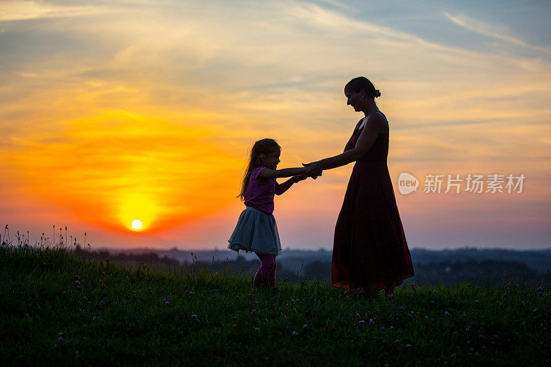 母亲和女儿在日落时在草地上玩耍