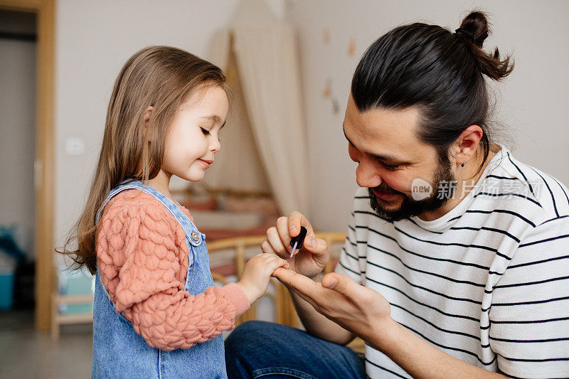 年轻的父亲在家给小女儿涂指甲
