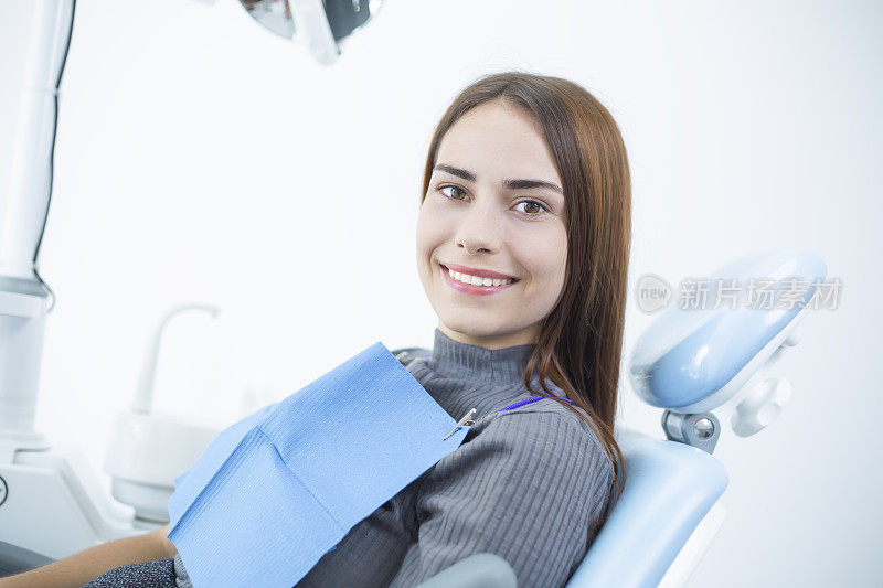 一位牙齿洁白、笑容灿烂的年轻女子坐在牙科诊疗室的椅子上。