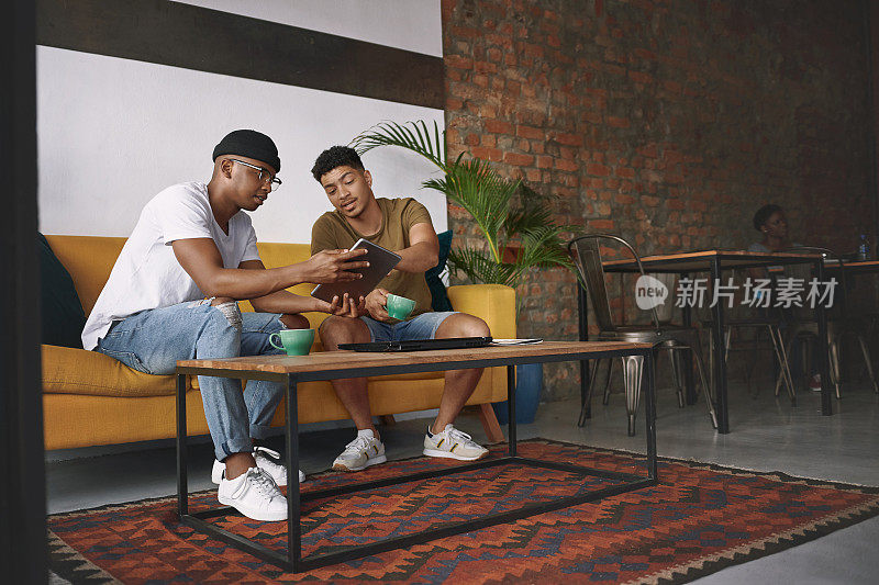 这张照片拍摄的是两个年轻人一起坐在咖啡店里用平板电脑聊天