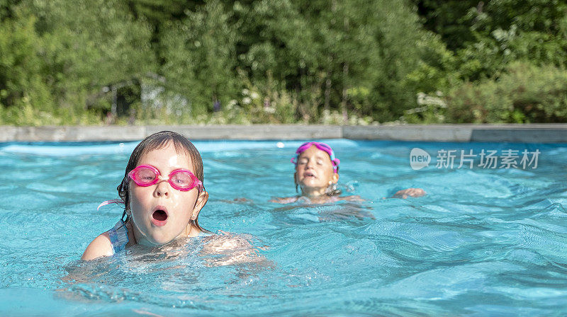 女孩们，白人孩子们，在房子后院的室外游泳池里游泳。