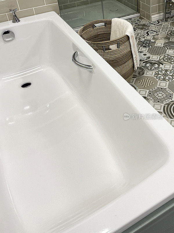近景现代浴室与白色，陶瓷浴缸与铬水龙头和把手，柳条洗衣篮，独立淋浴间与玻璃面板门，光泽，棕色瓷砖