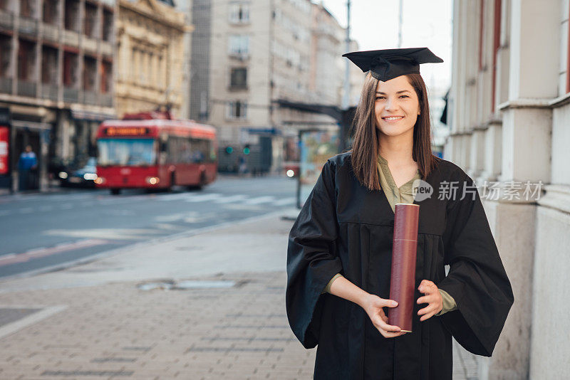 美丽的毕业生拿着毕业证书站在她的大学前面