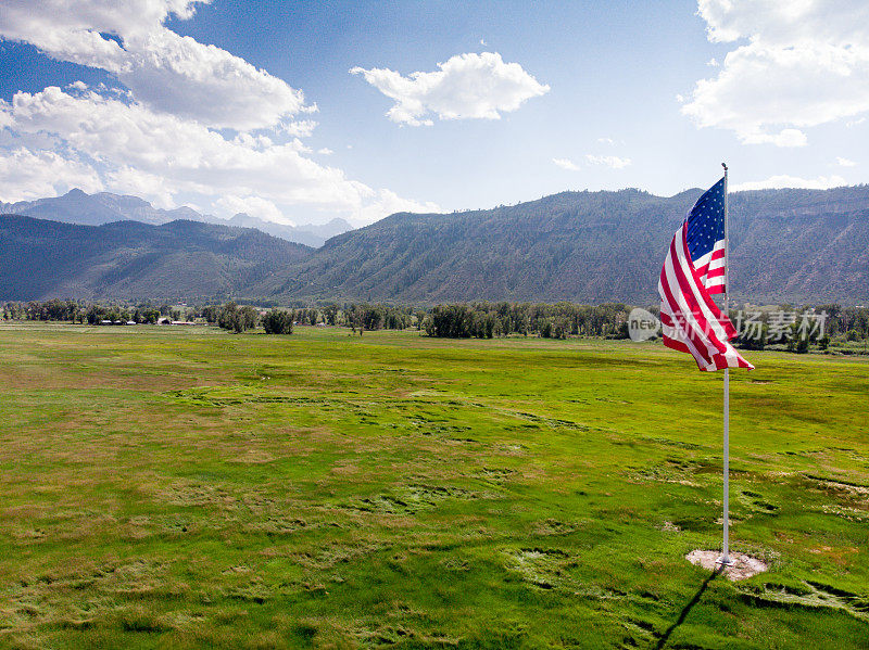美国国旗在科罗拉多州西南部靠近特柳赖德和乌雷的岩石山脉的草地上飘扬，这是一个晴朗的多云的日子，云层美丽