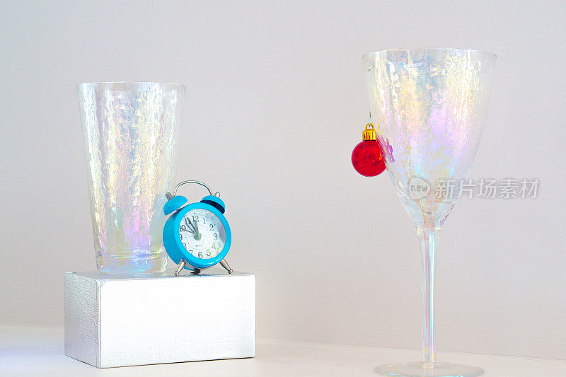 时尚的圣诞背景为光节日的设计构图红色的圣诞球，蓝色的时钟显示五到午夜，酒杯，礼盒