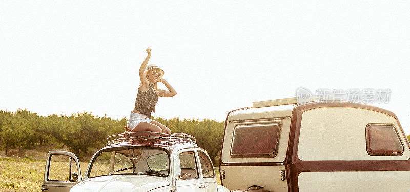 快乐的年轻女子在一个老式汽车屋顶和一个拖车寻找冒险的假期