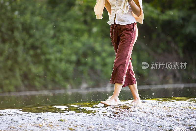 在流动的水中赤脚行走的年轻女子的低剖面