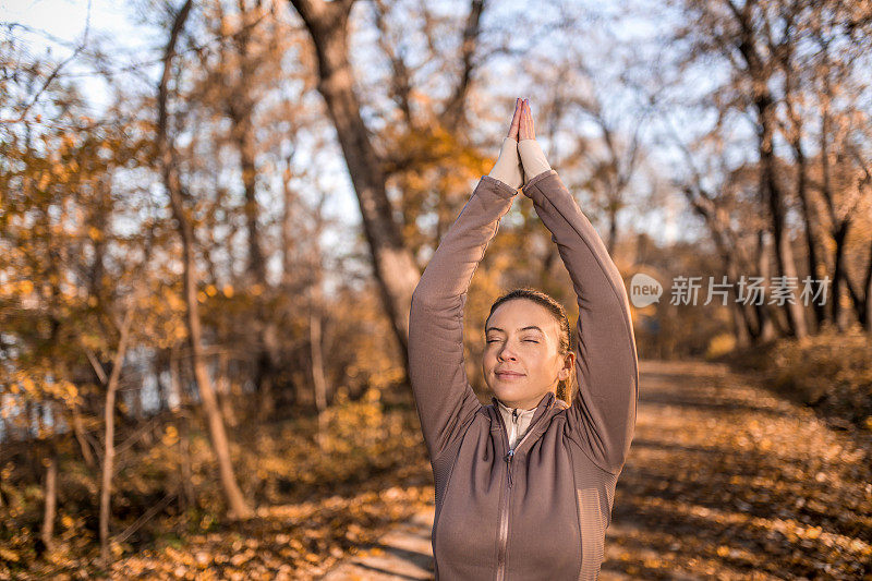 快乐的年轻女运动员在秋天的一天在公园里做瑜伽。