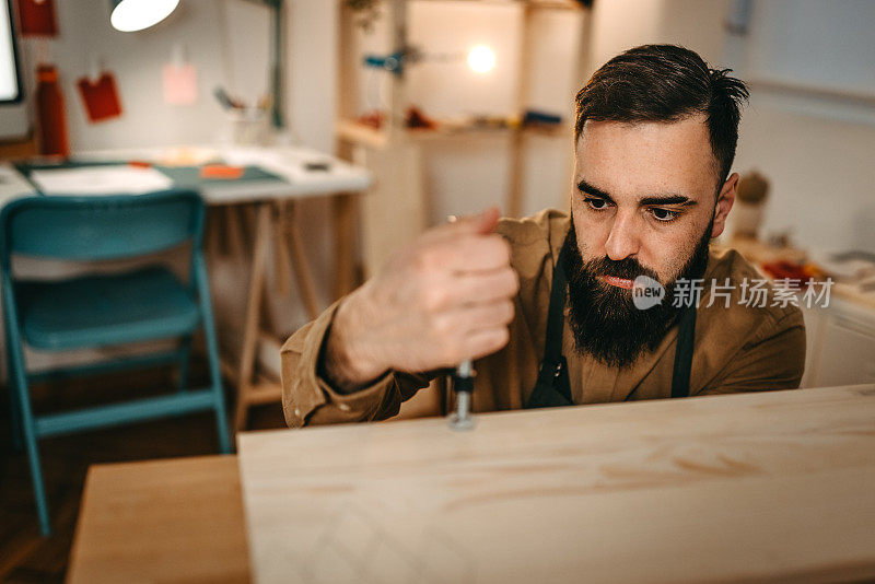 在艺术工作室里，留着胡子的男性艺术家在木头上拿着手工具