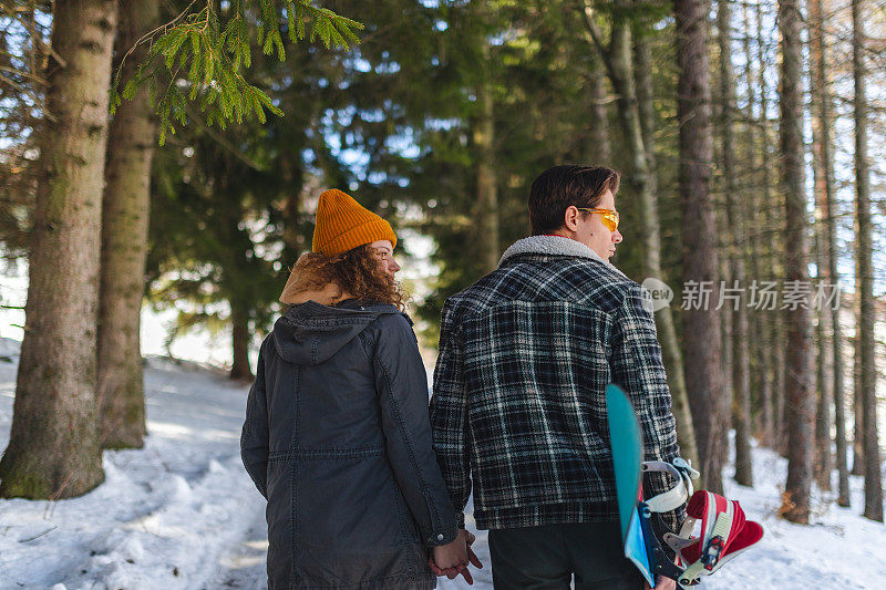 一对年轻的异性恋情侣手牵着手走过雪原森林