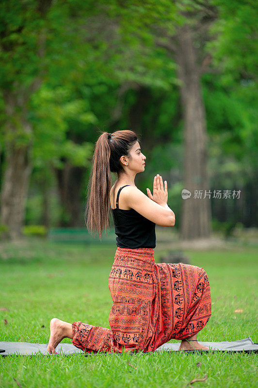 年轻女子做瑜伽体式与合十礼的姿势，而坐在地面上的公园