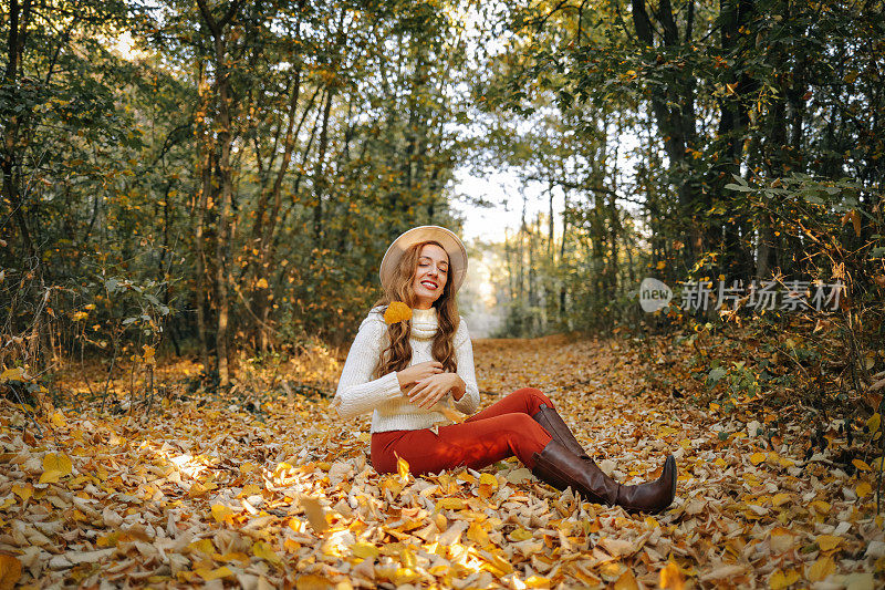 在阳光灿烂的日子里，微笑着的卷发女人在秋天的森林里扔树叶