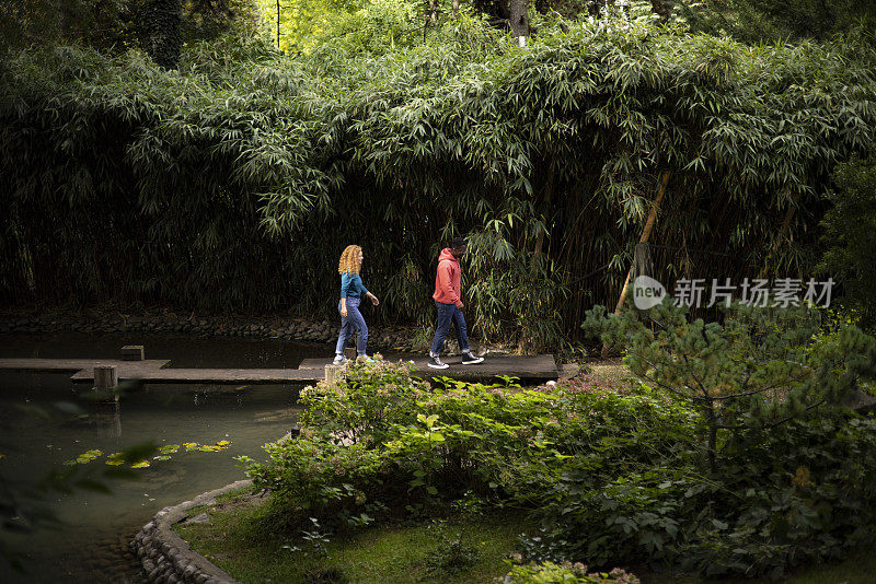 年轻的朋友们穿过植物园的木桥，在植物的环绕下穿过湖面