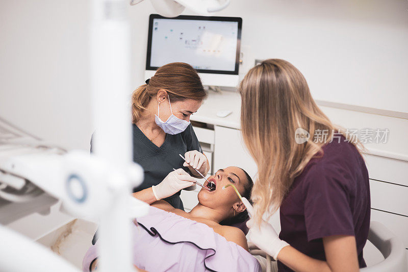 一位女牙医和她的助手坐在牙医椅上检查病人的牙齿。卫生员使用电气设备或空气涡轮机。口腔护理理念，清洁牙齿。