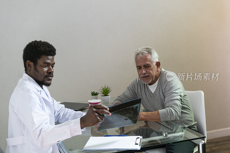 黑人男性牙医向老年病人展示全景颌片