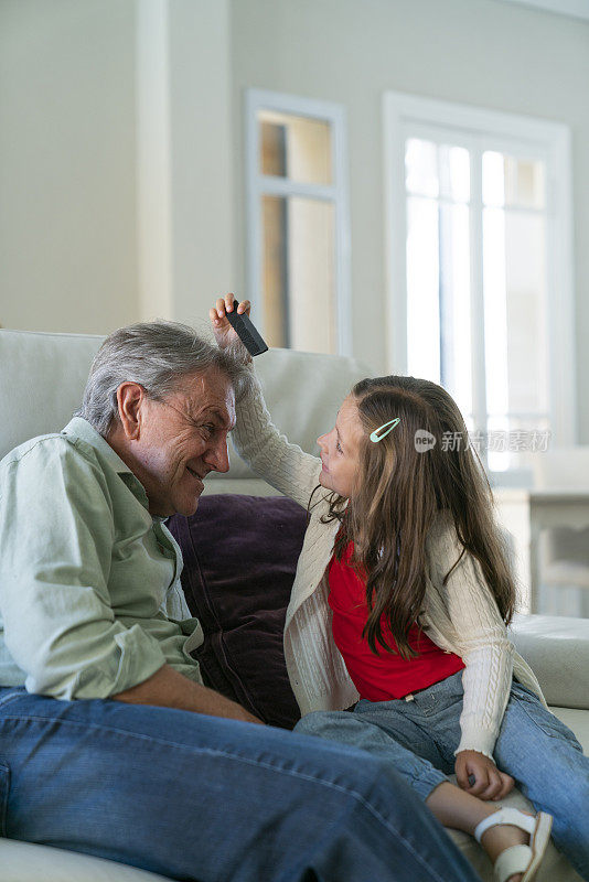 小女孩在家里的沙发上调皮地给爷爷梳头发