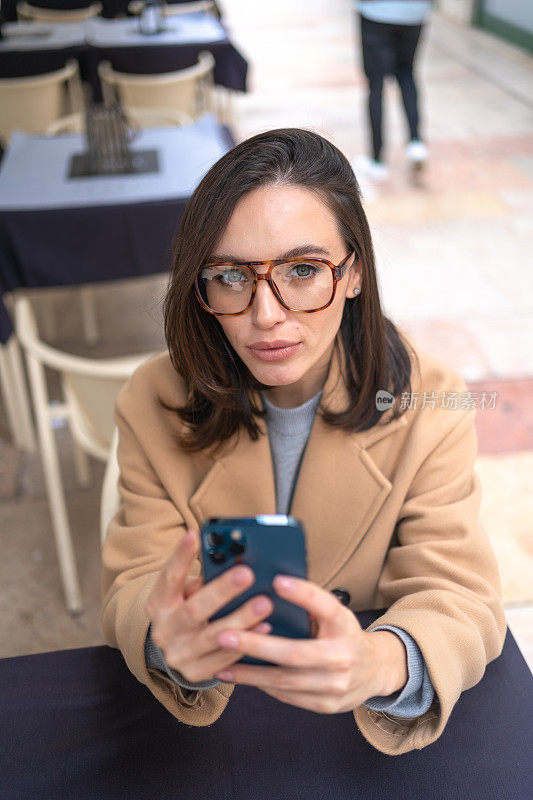 中年妇女坐在户外咖啡馆使用智能手机