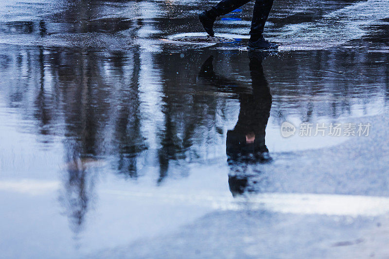 柏油路上的水坑。多雨的天气。下雨了。人的轮廓