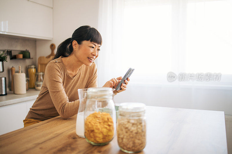 日本中年女性在厨房吃早餐时查看社交媒体的侧视图。