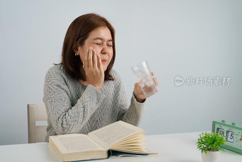 年轻的亚洲女子喝加冰的水，摸自己的脸颊，忍受牙痛，对寒冷有情绪反应。