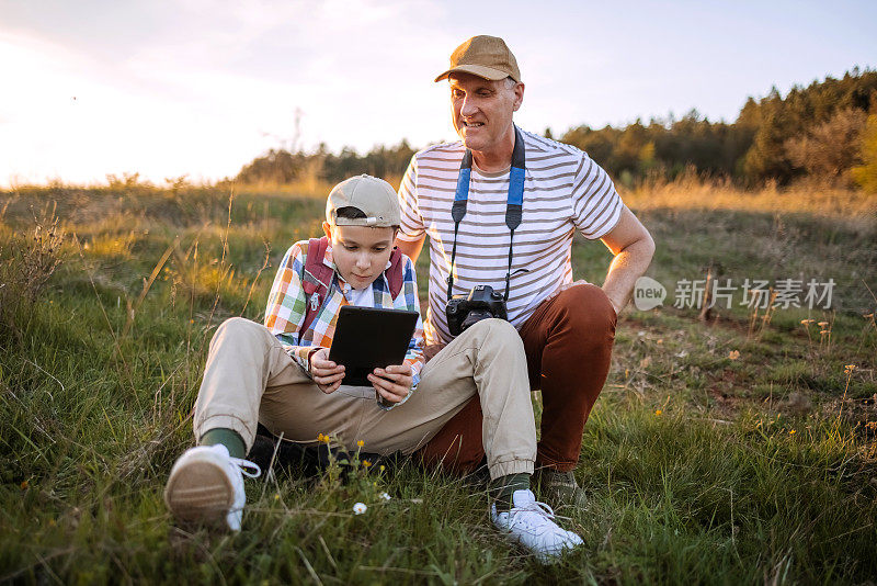 父亲和儿子在春天漫步在大自然中，用数码平板电脑拍摄珍贵的花朵