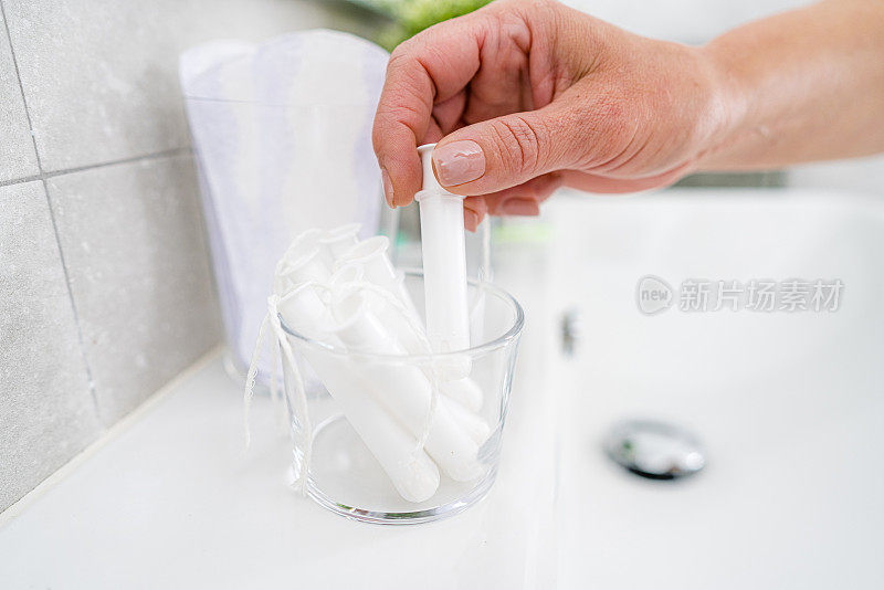 一个女人用手从浴室水槽里捡卫生棉条的特写