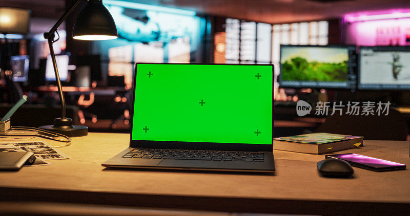 笔记本电脑绿屏模型站在木桌上。在背景时尚的现代办公室工作室在霓虹灯的晚上。创意设计师办公桌