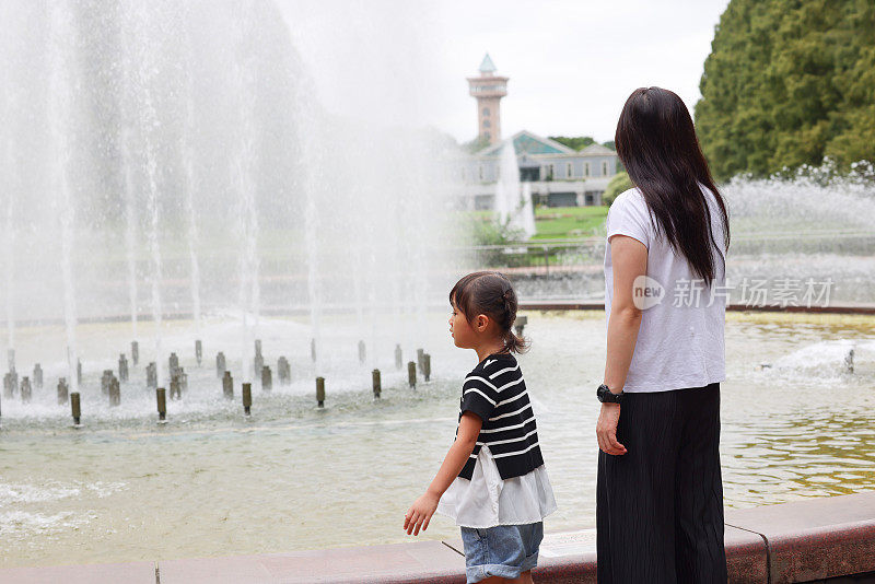 年轻的母亲和她的女儿在公园喷泉旁玩耍
