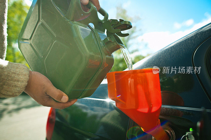 一个拿着汽油罐的人正在往他的汽车油箱里加油