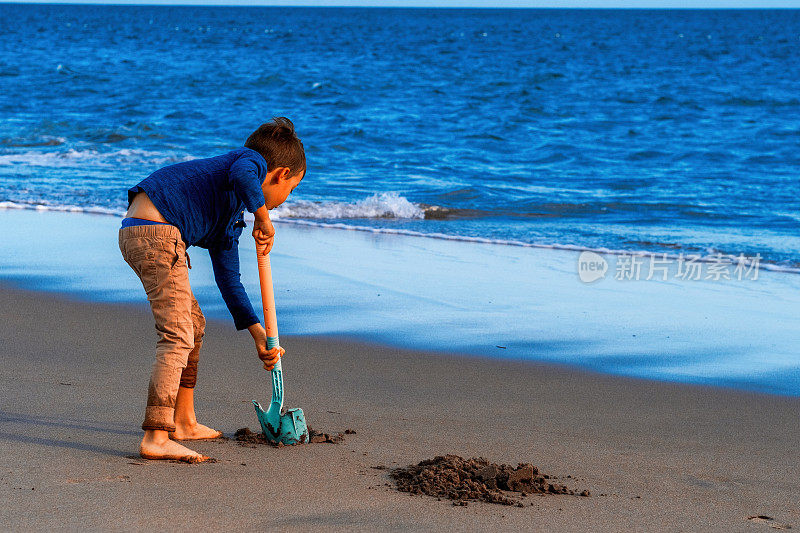 小男孩在沙滩上用铲子在沙地上挖洞
