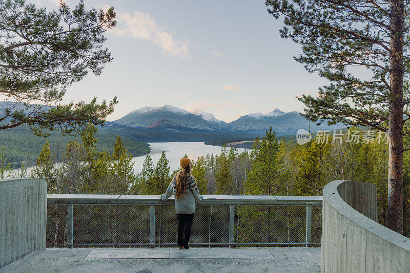 一位穿着羊毛衫的妇女凝视着日落，俯瞰着挪威的湖泊和山脉