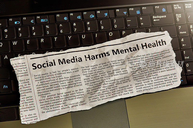 笔记本电脑键盘上的报纸剪报，标题和关于社交媒体危害心理健康的文章