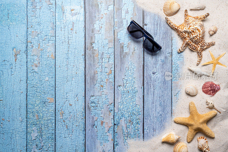 夏天，海滩和度假的概念与自由文本空间。前视图。平面布局与太阳眼镜，大海星和海贝壳和各种海贝壳和细沙滩在一个古老的蓝色木板背景