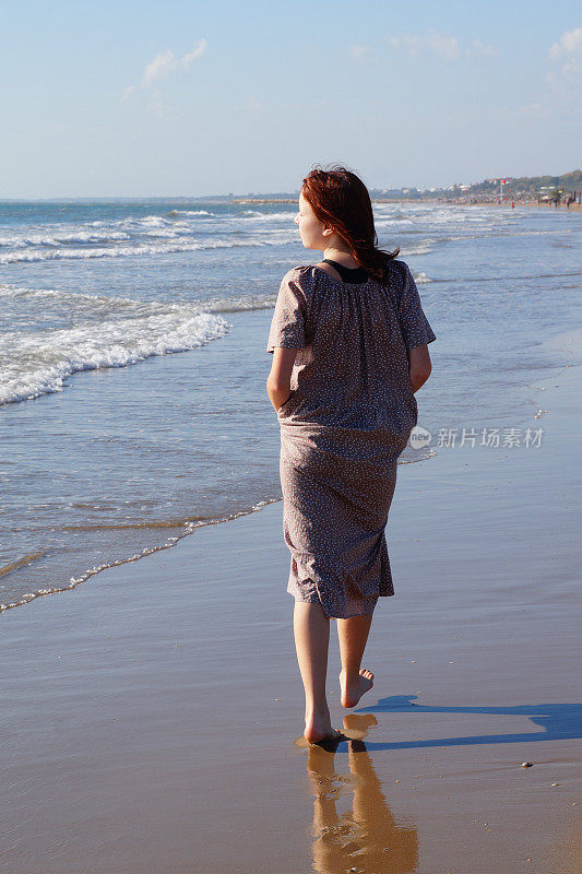 一个红头发的赤脚少女沿着海滨沿着水边走着