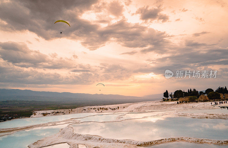 在丹尼兹利的日落时分，一架滑翔伞飞过Pamukkale的石灰华池和Hierapolis