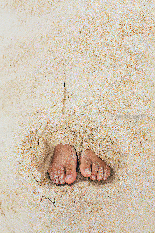 小女孩的脚埋在沙子里，小女孩正在沙滩上玩耍
