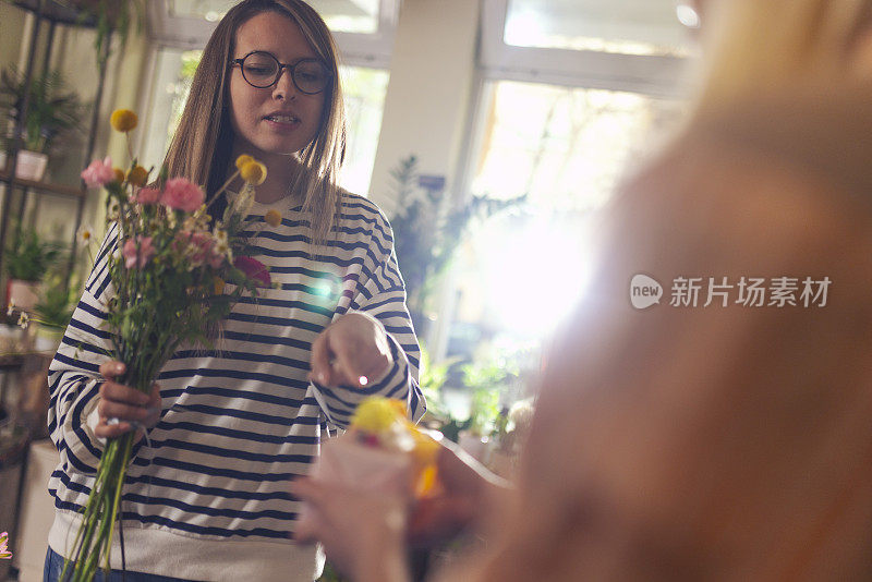 一位女顾客正在一家花店购物，正在挑选她想让花店老板用哪种花来制作花束