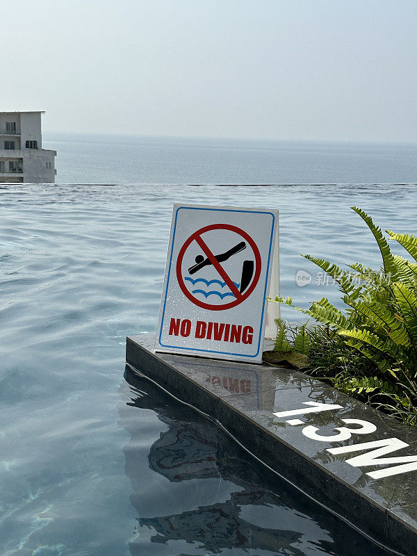 “禁止潜水”标志的特写图像，建议a框夹心板，室外闪亮的抛光混凝土泳池边，无限游泳池深度标记，重点在前景