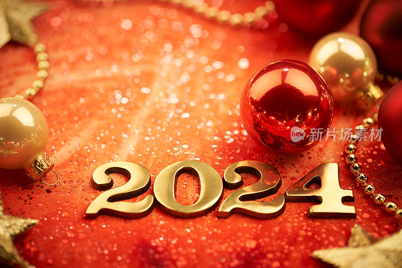 2024年新年快乐!红色背景上的金色数字和圣诞装饰。