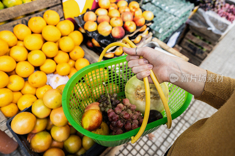 在街边的杂货店里，一位顾客举着购物篮挑选水果和蔬菜的特写